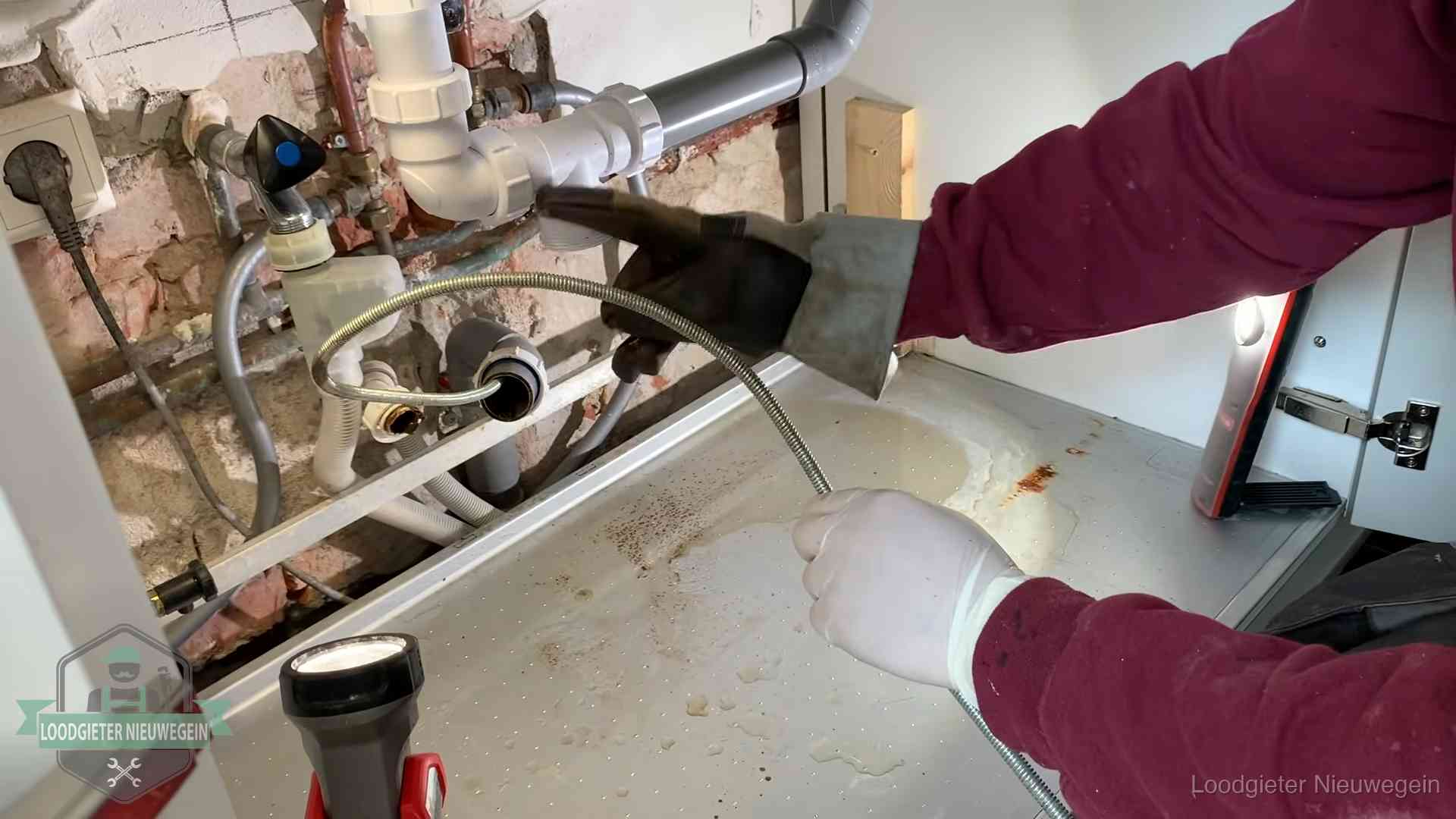 Ontstoppingsveer gaat in een geopende sifonaansluiting onder het aanrecht in Nieuwegein