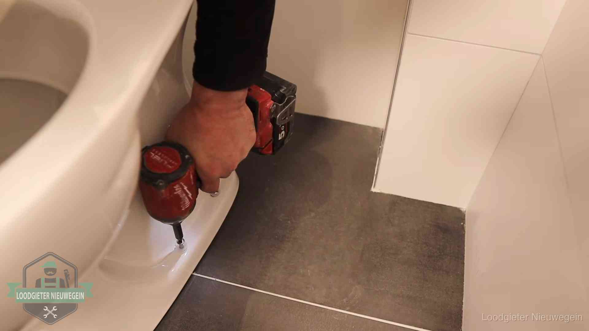 Loodgieter zet de voet van een wc-pot vast op de tegelvloer in Nieuwegein